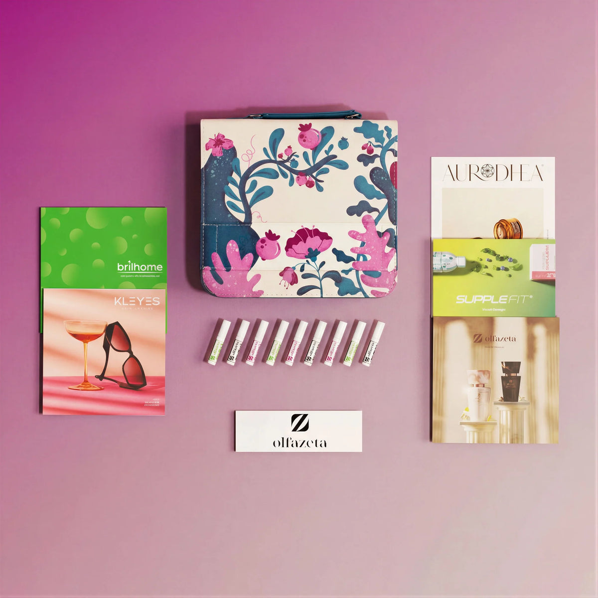 Kit de muestras Olfazeta by Chogan: viales, neceser de motivo floral y catálogos de marcas sobre fondo rosa malva
