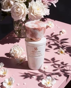 Frasco blanco Olfazeta by Chogan Millésime N°51 rodeado de rosas blancas, sombras de follaje al sol