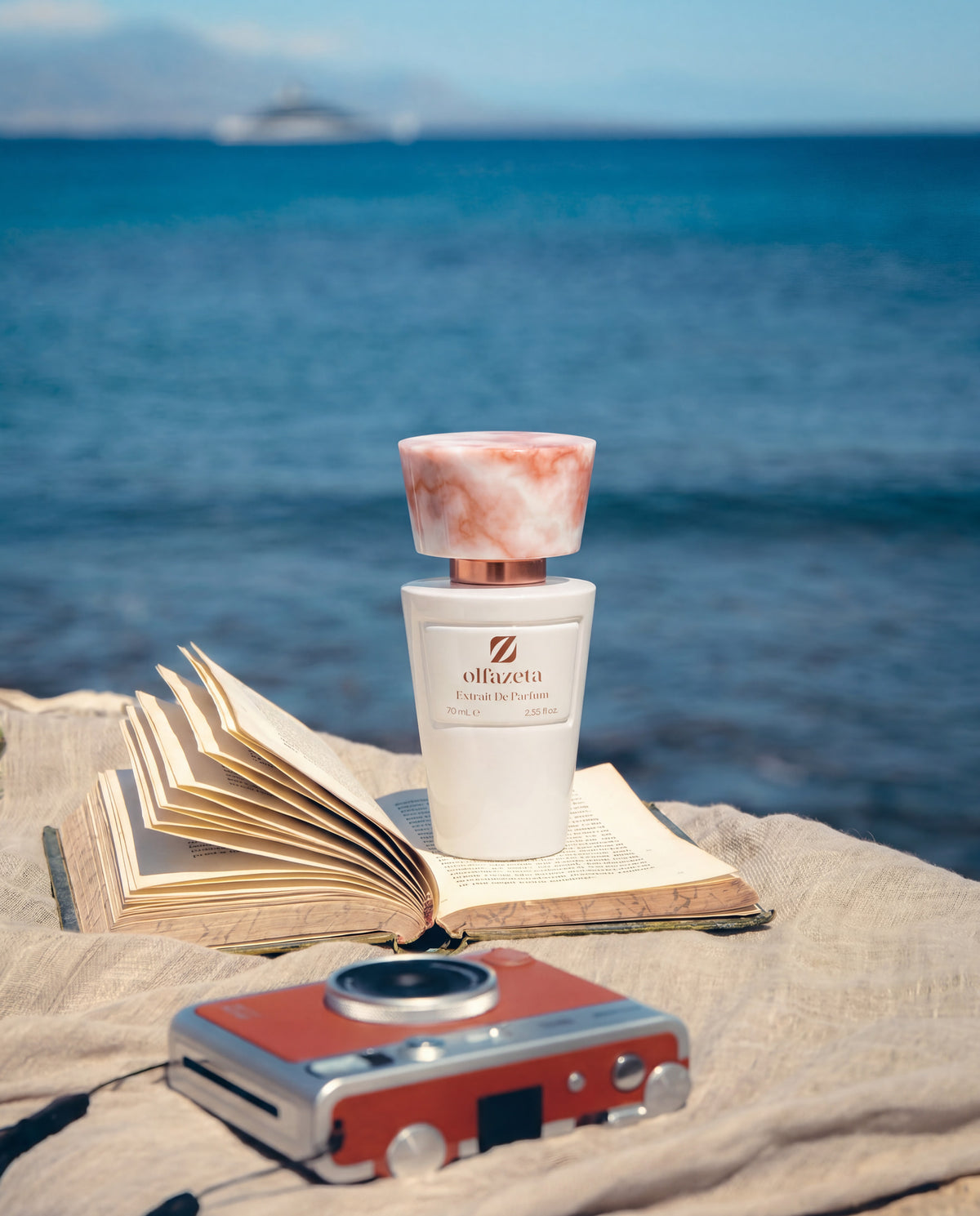 Witte flacon Olfazeta by Chogan Millésime N°29, roze gemarmerde dop, op een opengeslagen boek met uitzicht op zee